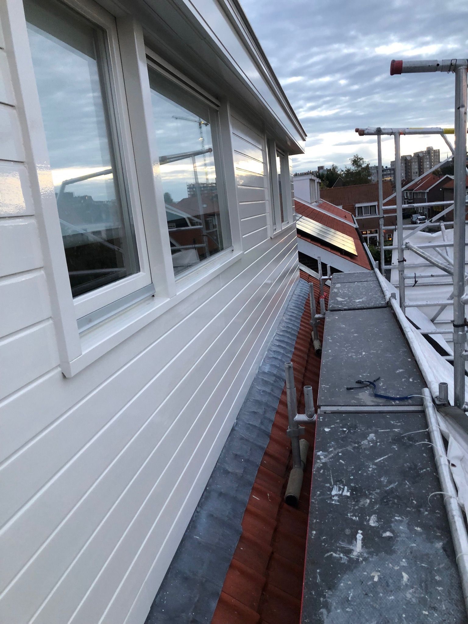 Witte gevelbekleding met ramen, rood dak en steigerwerk.