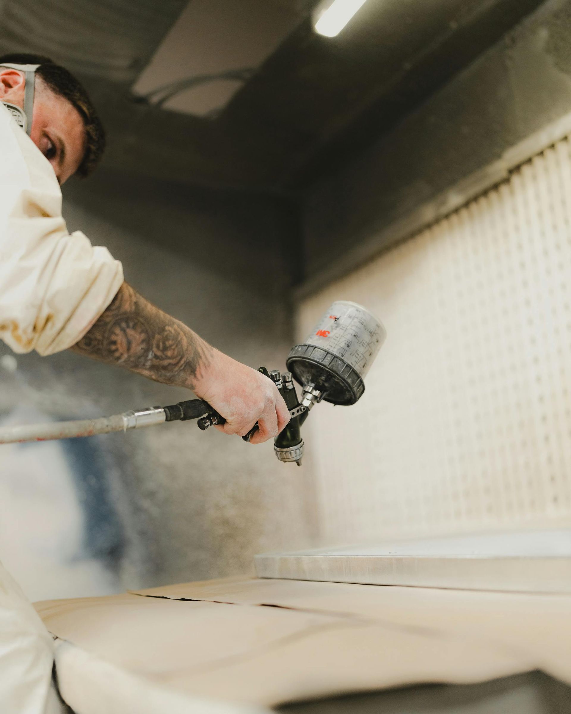 Persoon die hout spuit in een spuitcabine, draagt ​​een masker en beschermende kleding.
