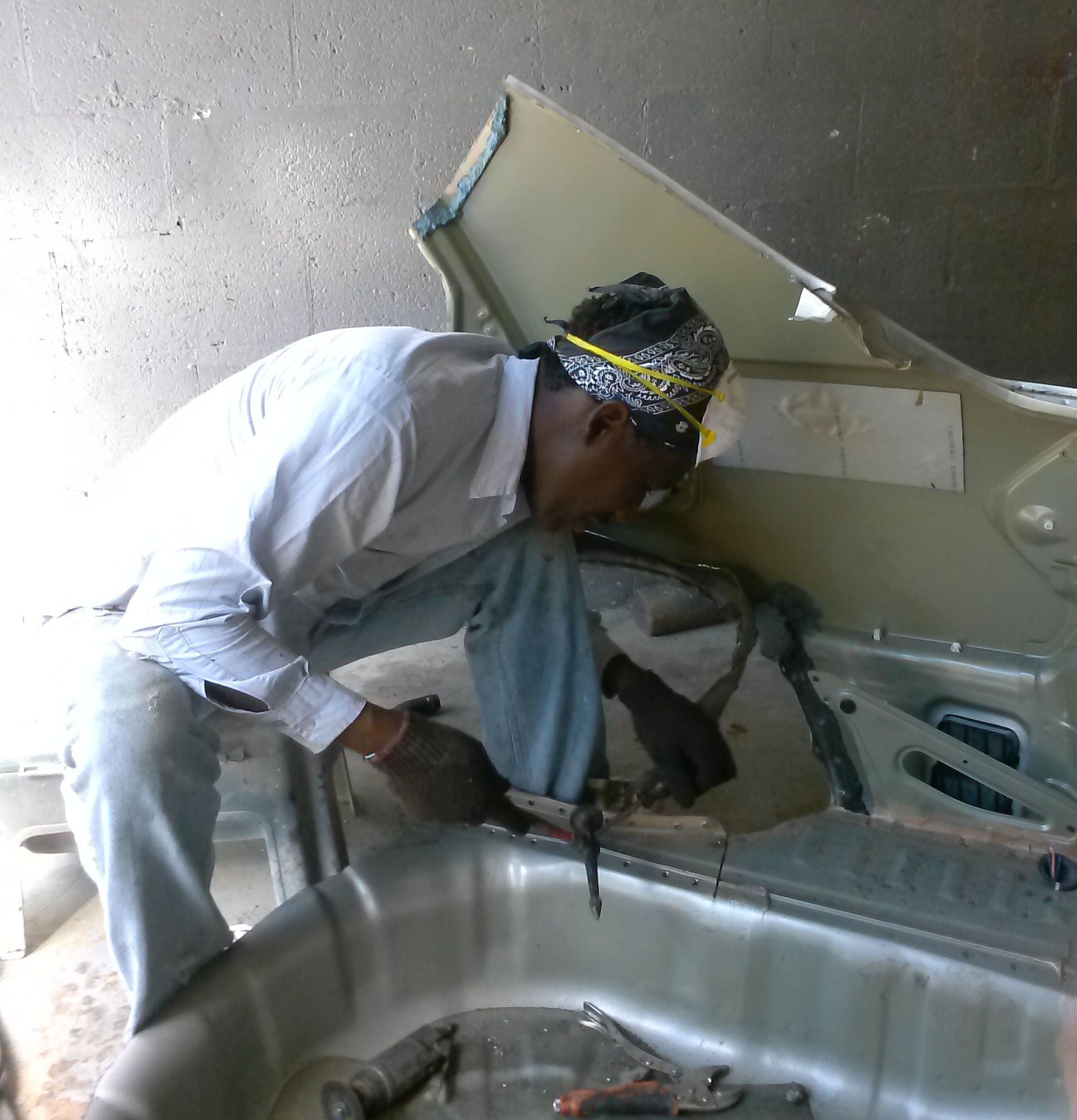 A man wearing a bandana is working on a car