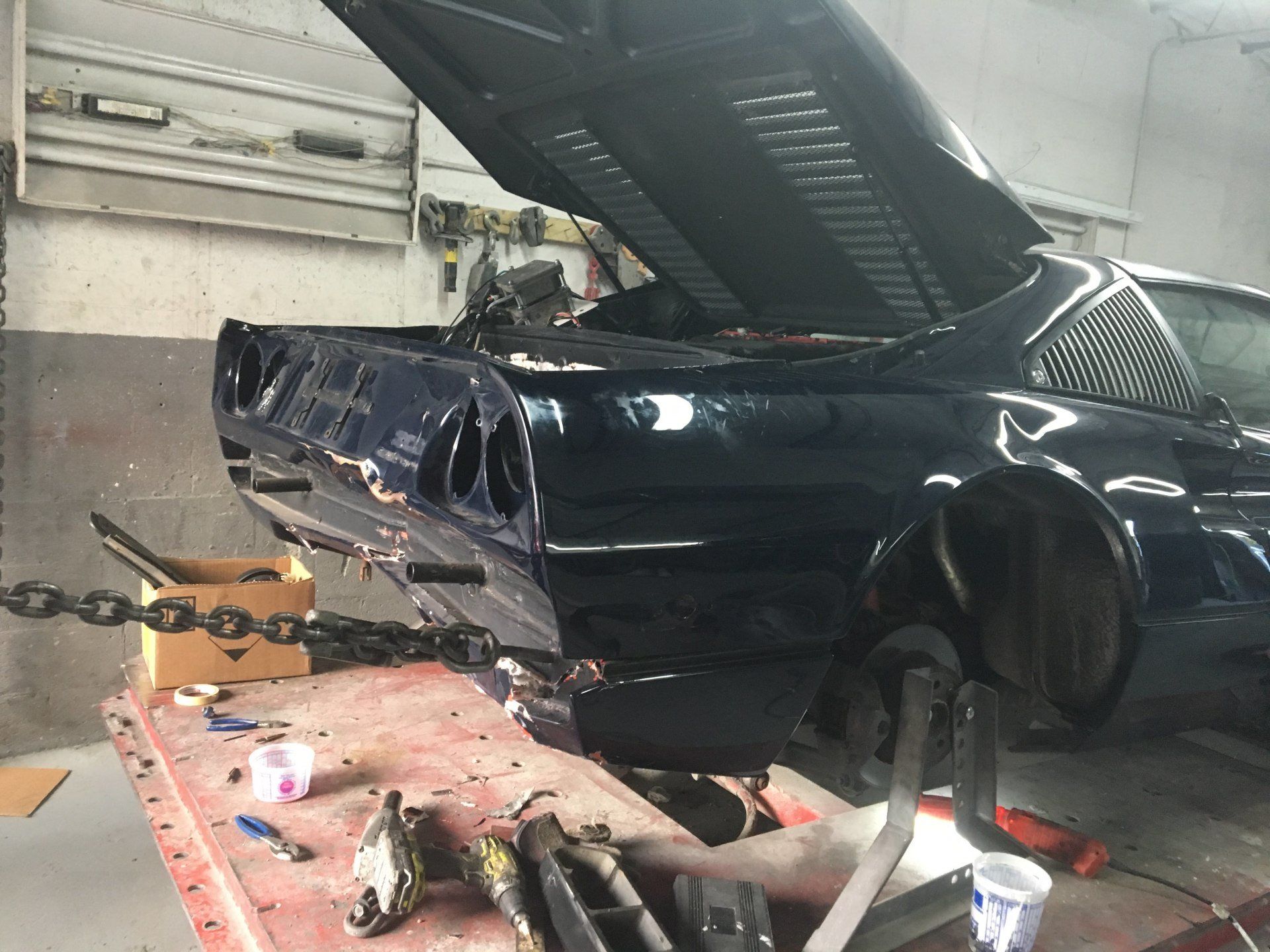 A blue car with the hood open is sitting on a table in a garage.
