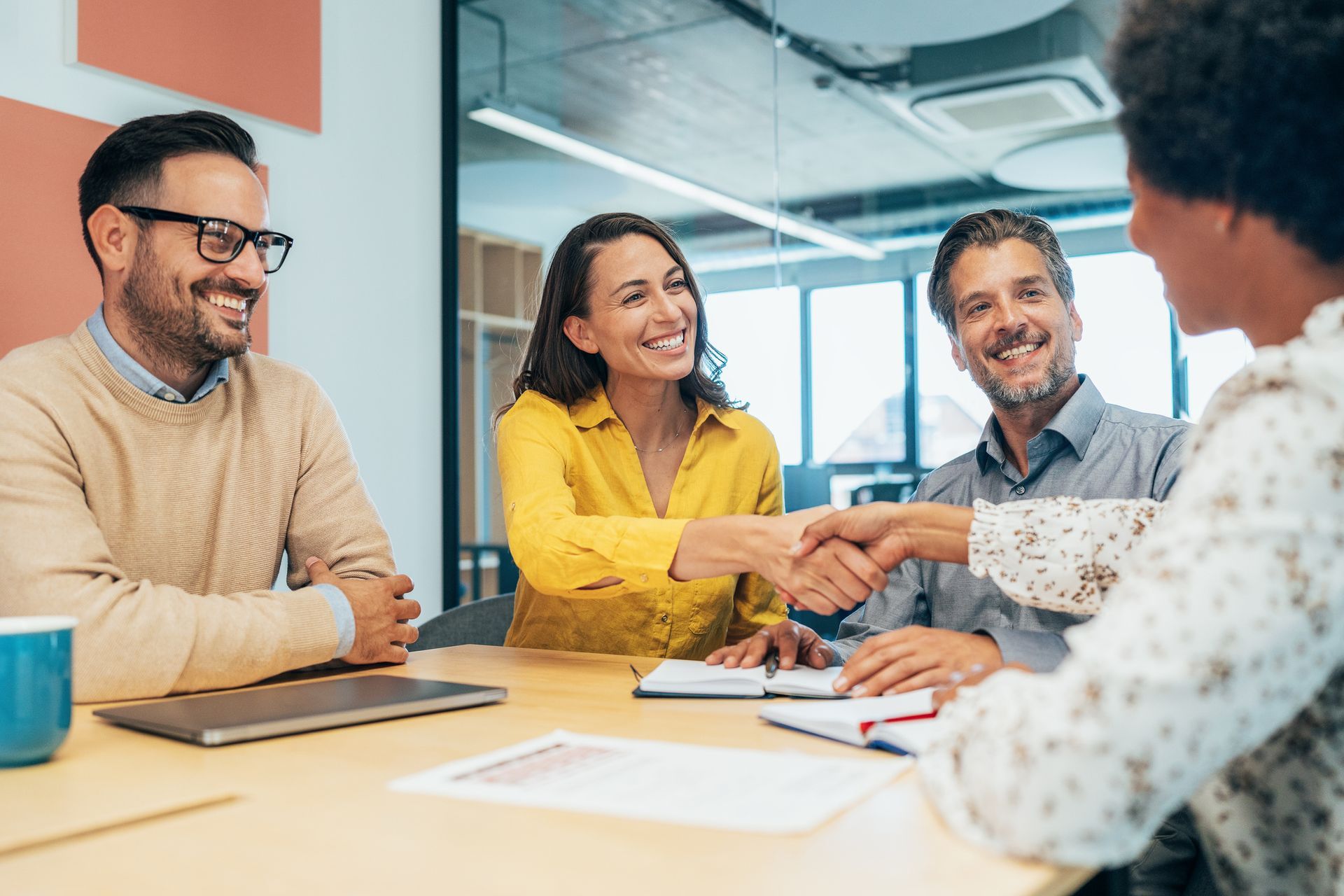 A group of people are shaking hands while sitting around a table.