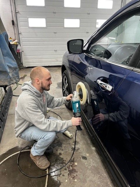 A man is polishing a blue car in a garage.
