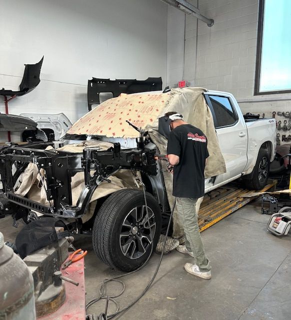 Mechanic welding a white pickup truck's front frame in a repair shop.