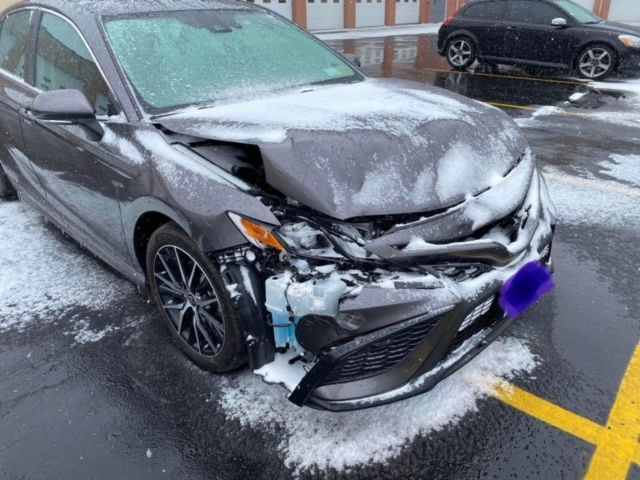 A gray car with a damaged front end is parked in a parking lot.