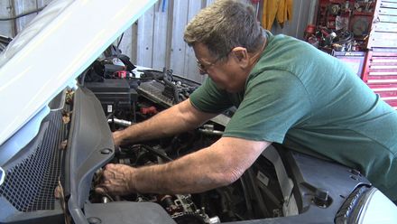 A man in a green shirt is working on the engine of a car.