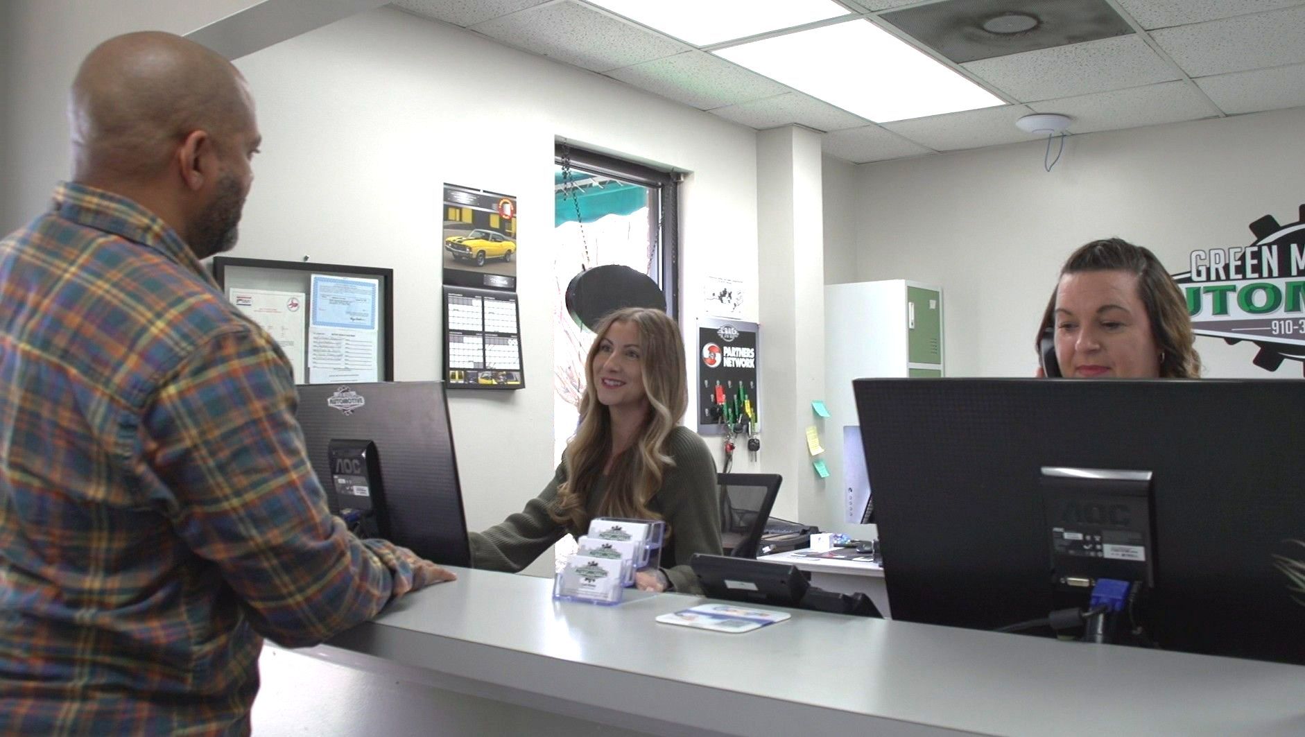 A man is standing at a counter in a car dealership talking to a woman.