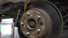A man is measuring the brake rotor of a car with a tape measure.
