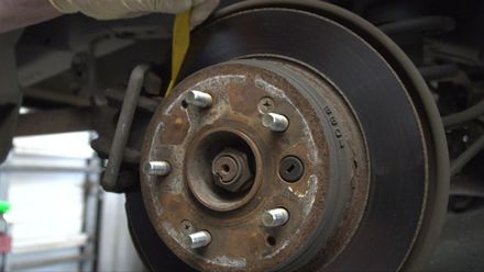 A man is measuring the brake rotor of a car with a tape measure.