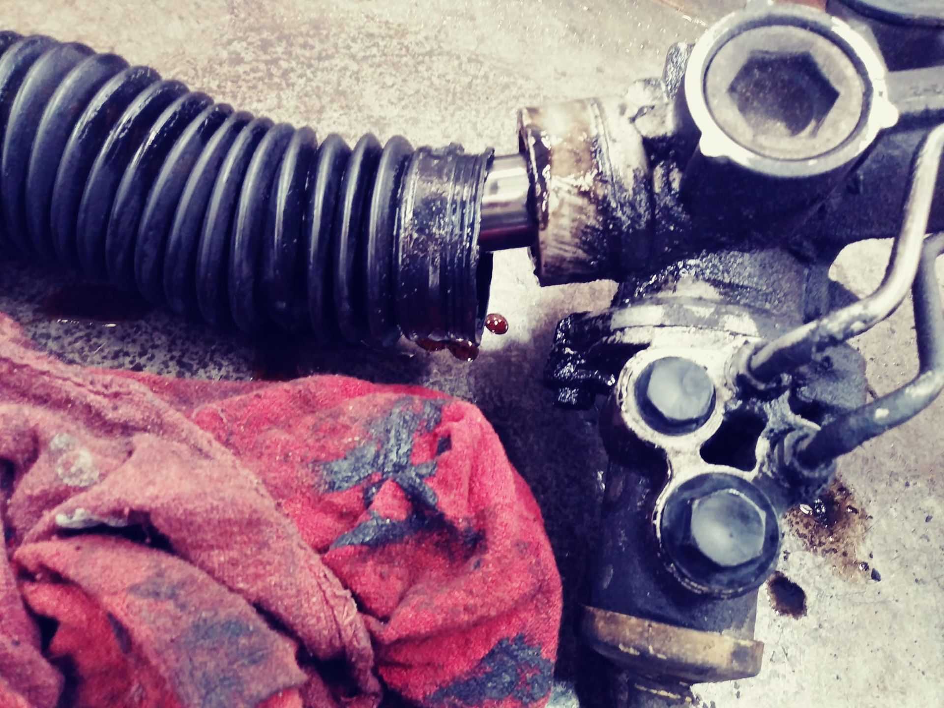 Leaky car steering rack with protective boot, red cloth, and dark fluid.