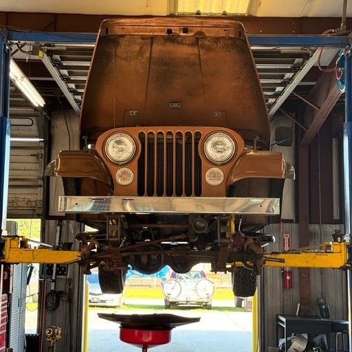 A vintage Jeep is raised on a car lift in a repair shop, with the hood open for maintenance.