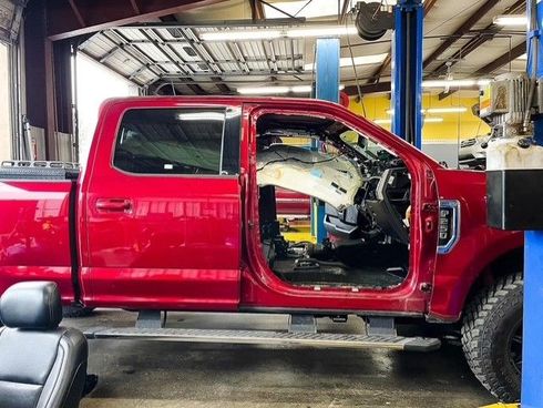 Red pickup truck in a repair shop with its door removed, showing deployed airbags and interior damage.