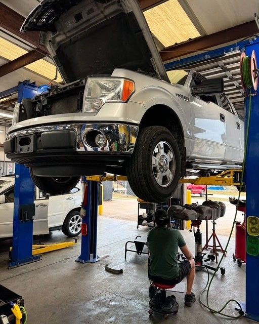 White pickup truck raised on a lift in a garage. A mechanic is working underneath.