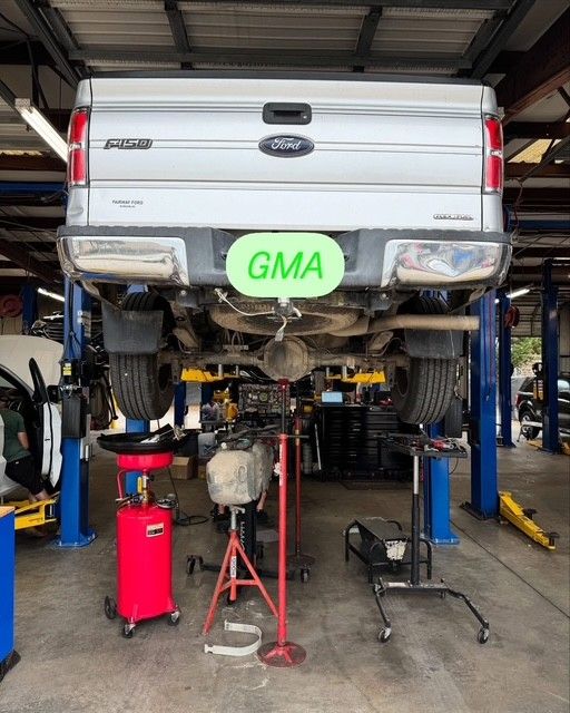 A silver Ford pickup truck raised on a lift in a garage for maintenance, showing its undercarriage. Tools and equipment surround the vehicle.