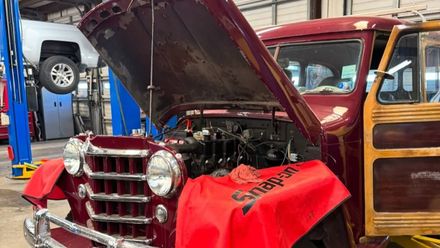 A red truck with the hood up is being worked on in a garage.