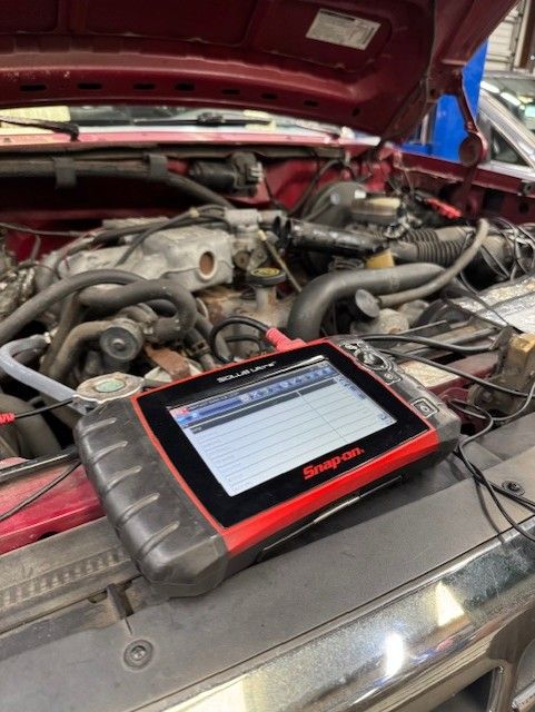 A Snap-on diagnostic scan tool rests on the front edge of a vehicle's open engine bay in a repair shop.
