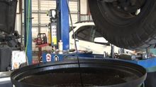A bucket of oil is being poured under a car