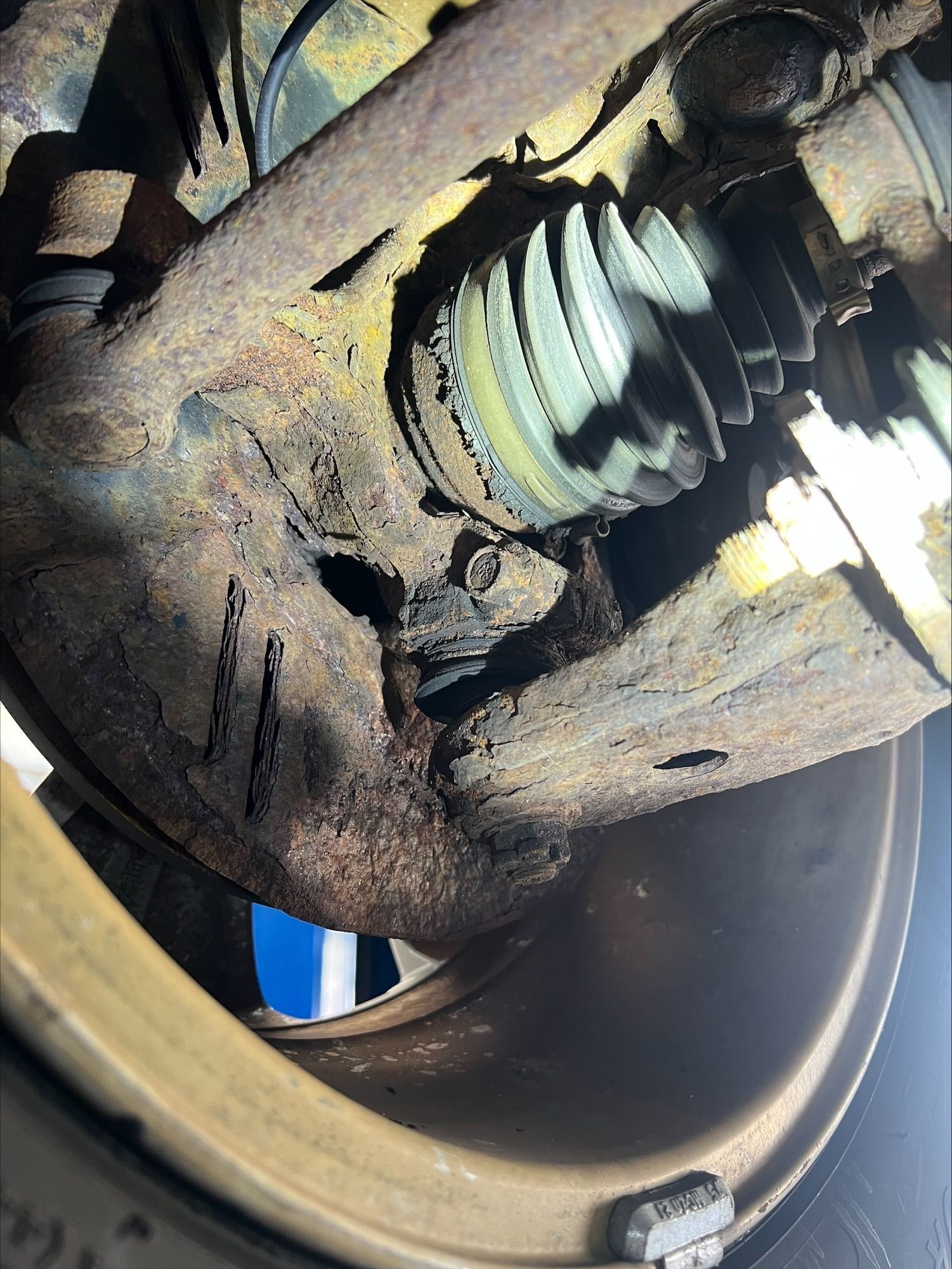 Close-up of a rusty damaged wheel hub with a torn CV joint boot and exposed axle shaft.