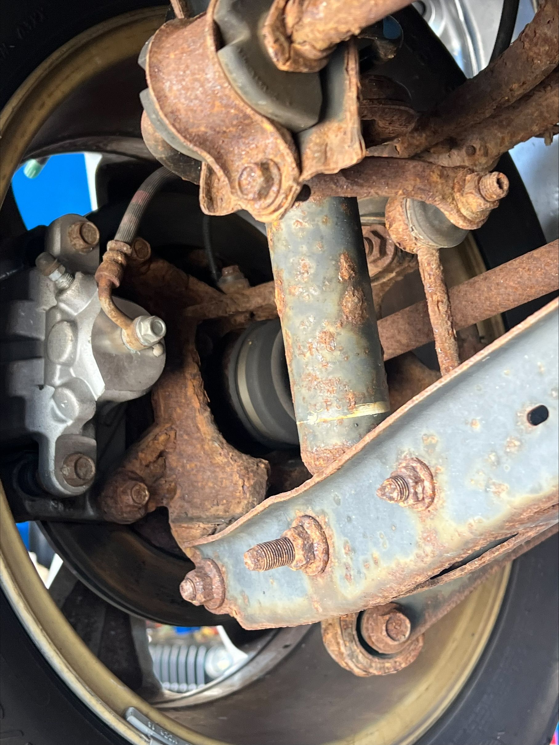 Rusty car wheel suspension and brake assembly close-up, showing corroded metal parts and wheel rim