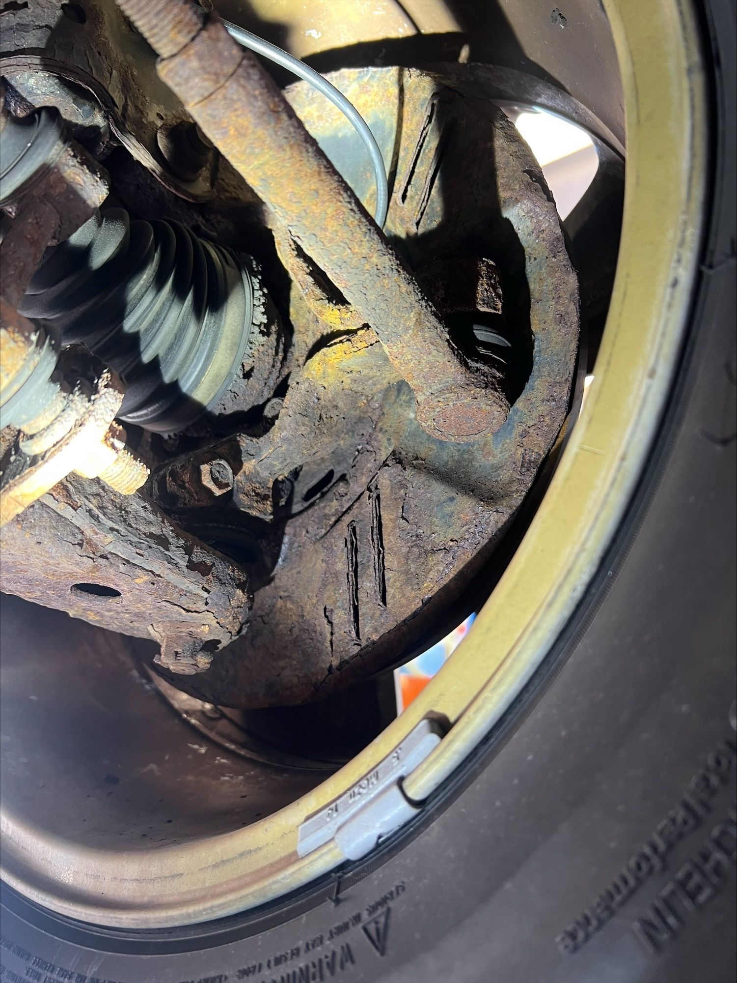 Close-up of a dusty car wheel rim and tire with visible suspension and brake components inside the wheel well