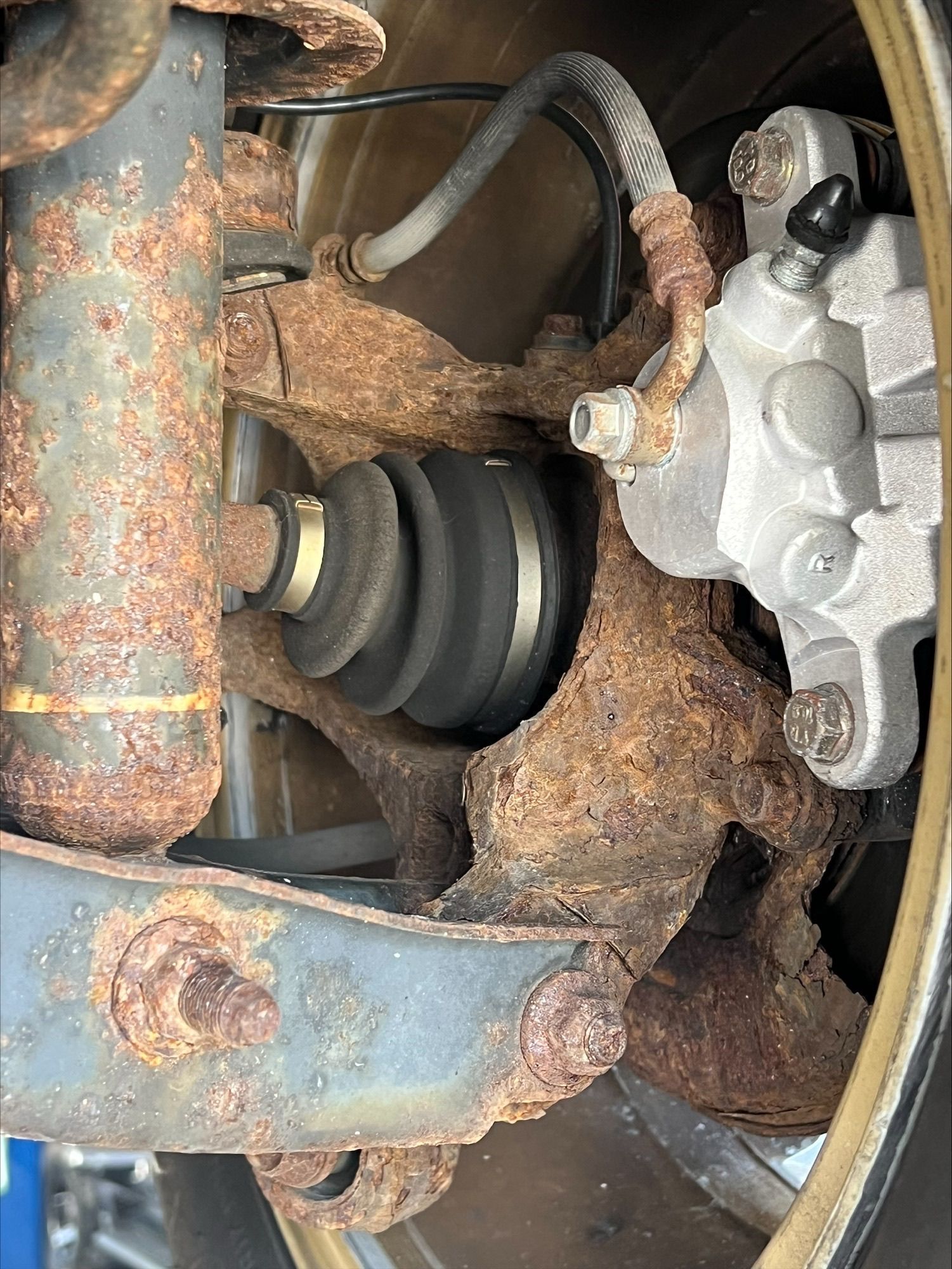 Close-up of a rusty car suspension with CV axle and brake caliper.