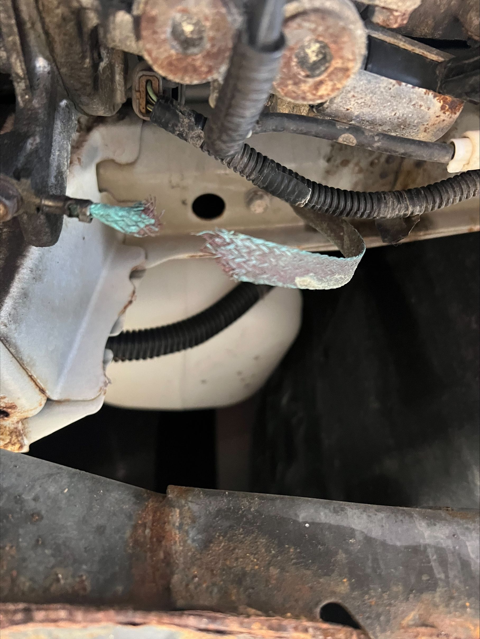 Close-up of damaged wiring and rusty metal brackets inside a machine compartment