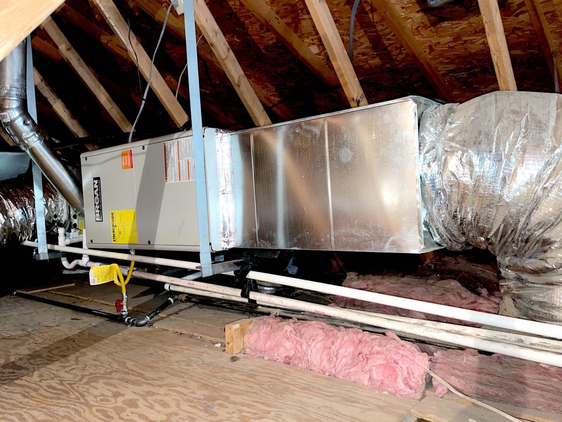 An air conditioner is hanging from the ceiling of an attic.