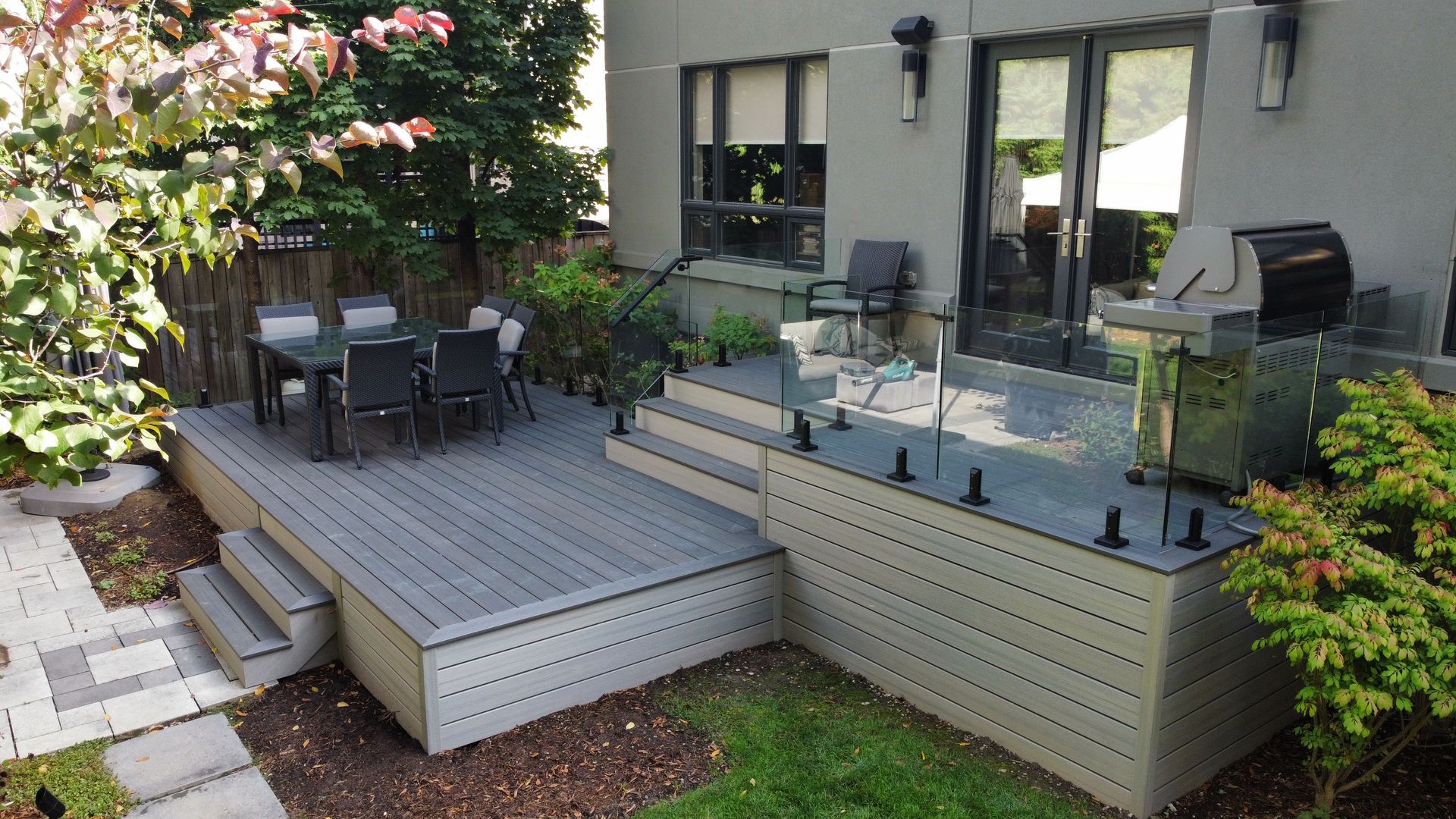 Wooden deck with outdoor dining table, steps, and barbecue grill in backyard setting.