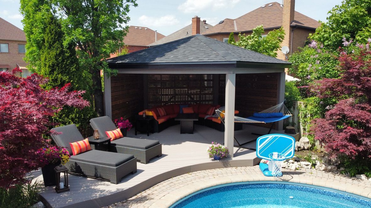 A pool deck with a covered pavilion featuring outdoor seating, lounge chairs, and a hammock beside a swimming pool.