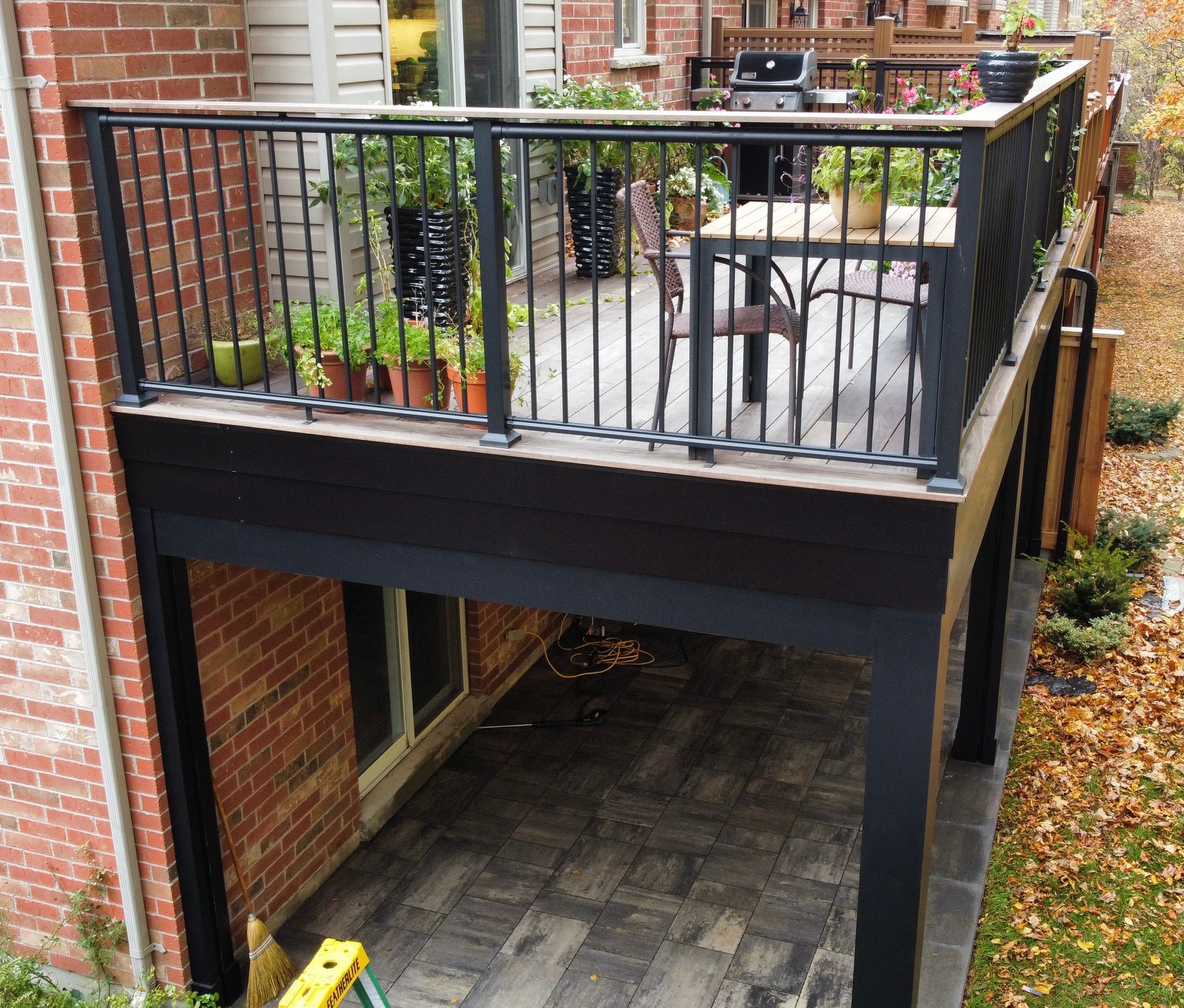Elevated black deck with metal railing, brick home exterior, and a patio underneath.