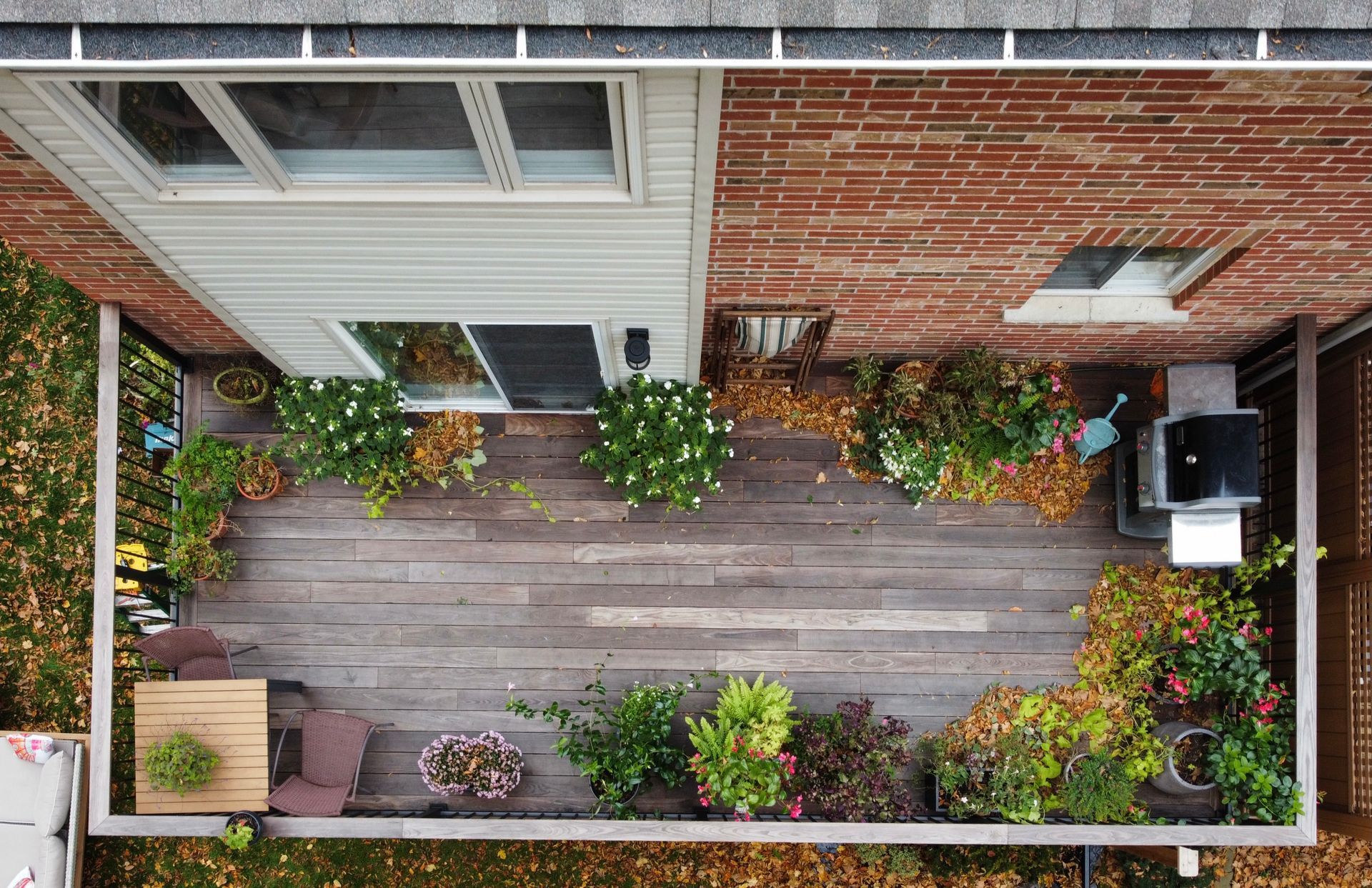 Aerial view of a deck with various potted plants, grill, and patio furniture next to a brick building.