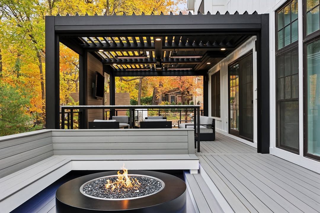 Modern deck with fire pit, pergola, built-in seating, and a backdrop of colorful fall foliage.