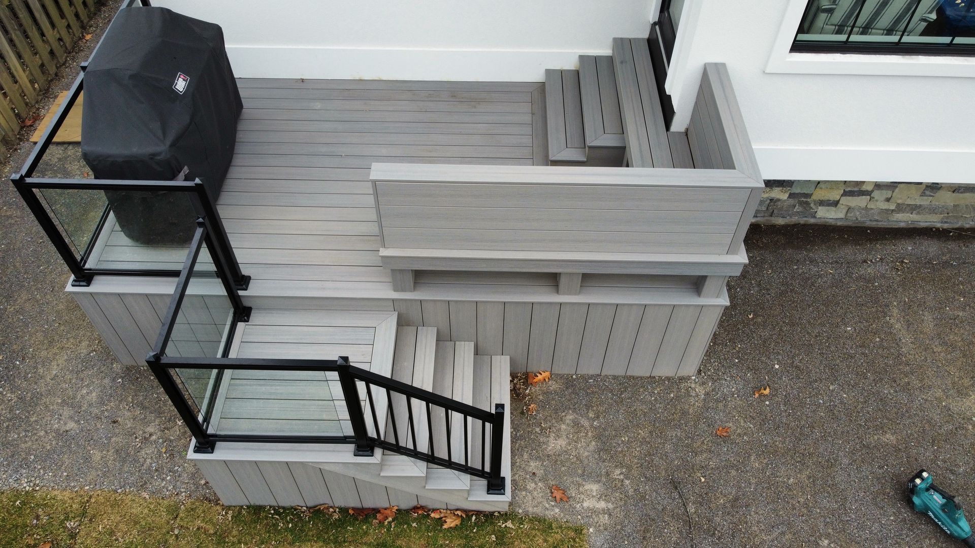 Gray composite deck with glass and black metal railings, grill, and stairs leading down to yard.