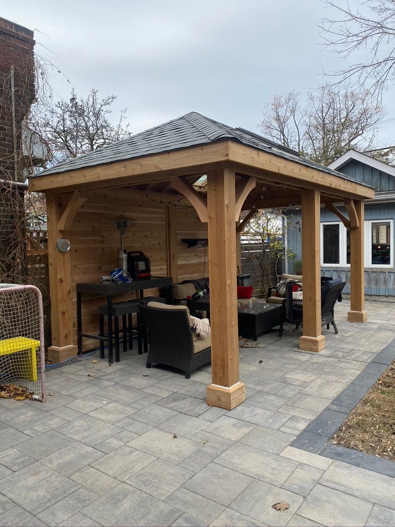 A wooden gazebo with a roof is sitting on top of a patio next to a house.