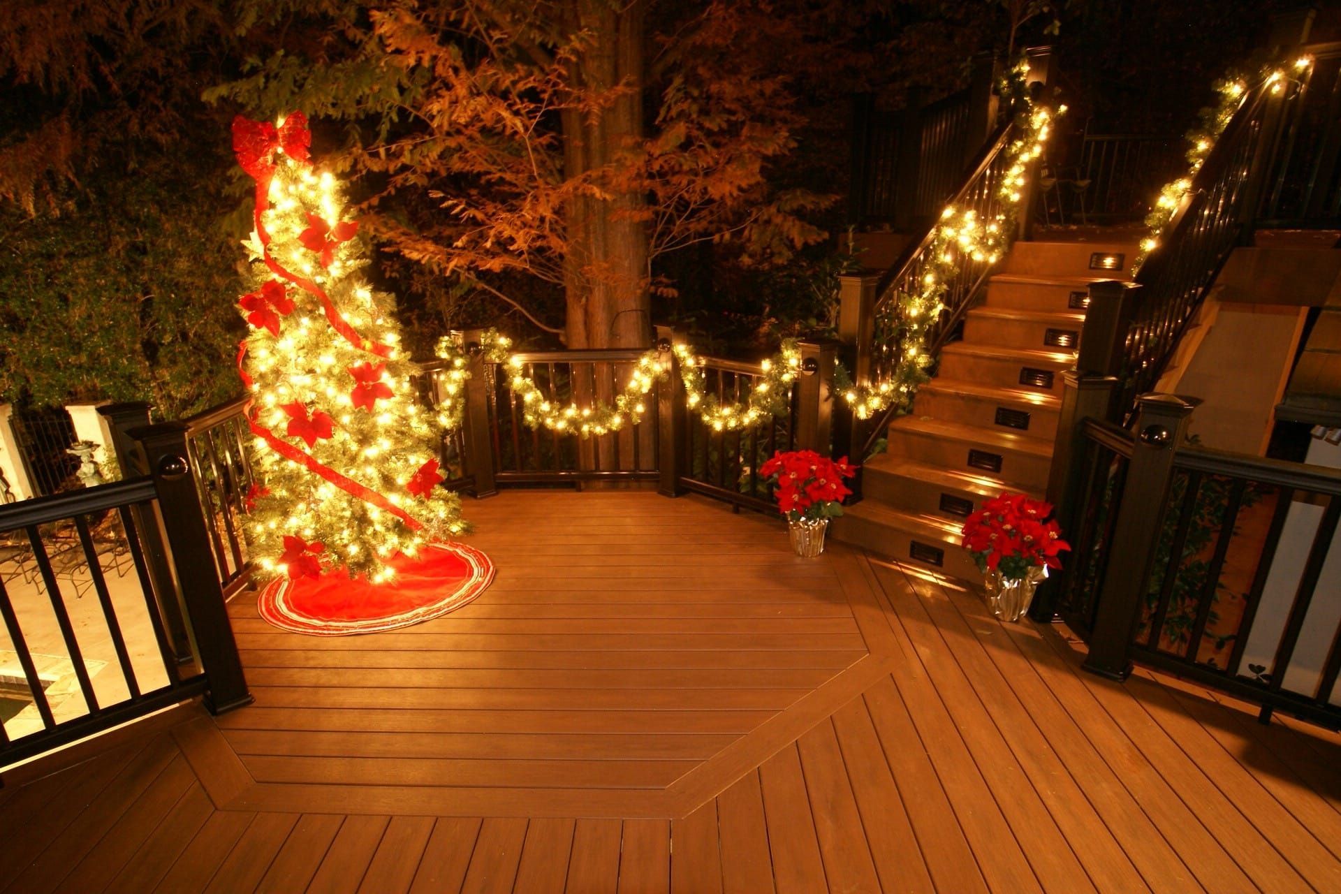 Deck decorated with Christmas lights, tree, and poinsettias at night.