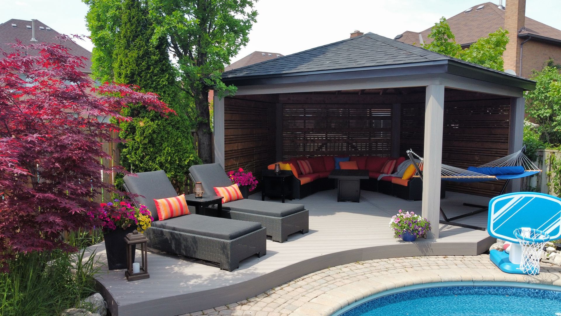 A backyard patio with a gazebo, lounge chairs, and a pool.