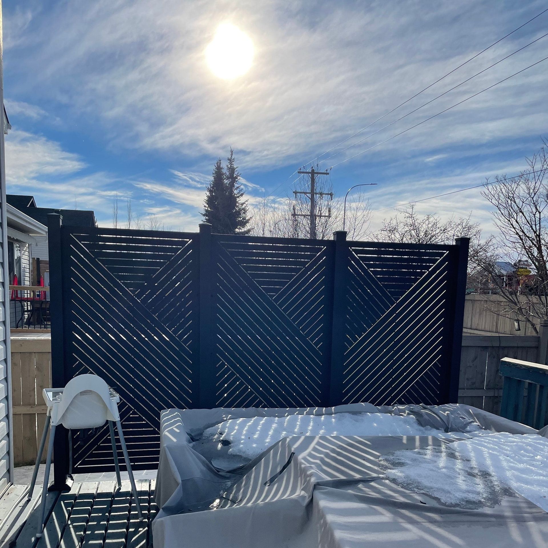 Backyard patio with black patterned privacy fence, covered hot tub, blue sky, and sun.