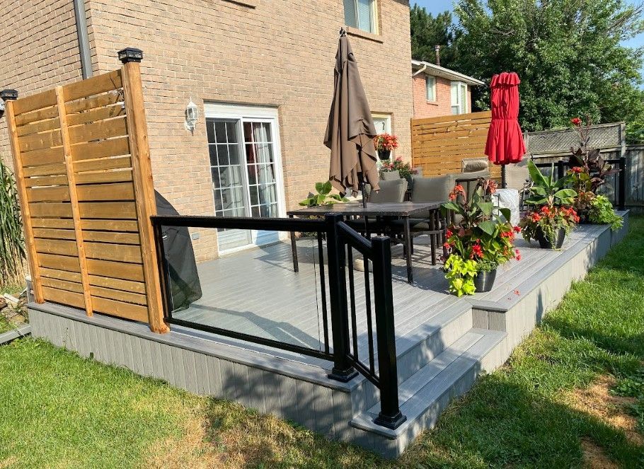 Backyard deck with glass railing, seating area, and wooden privacy screens.