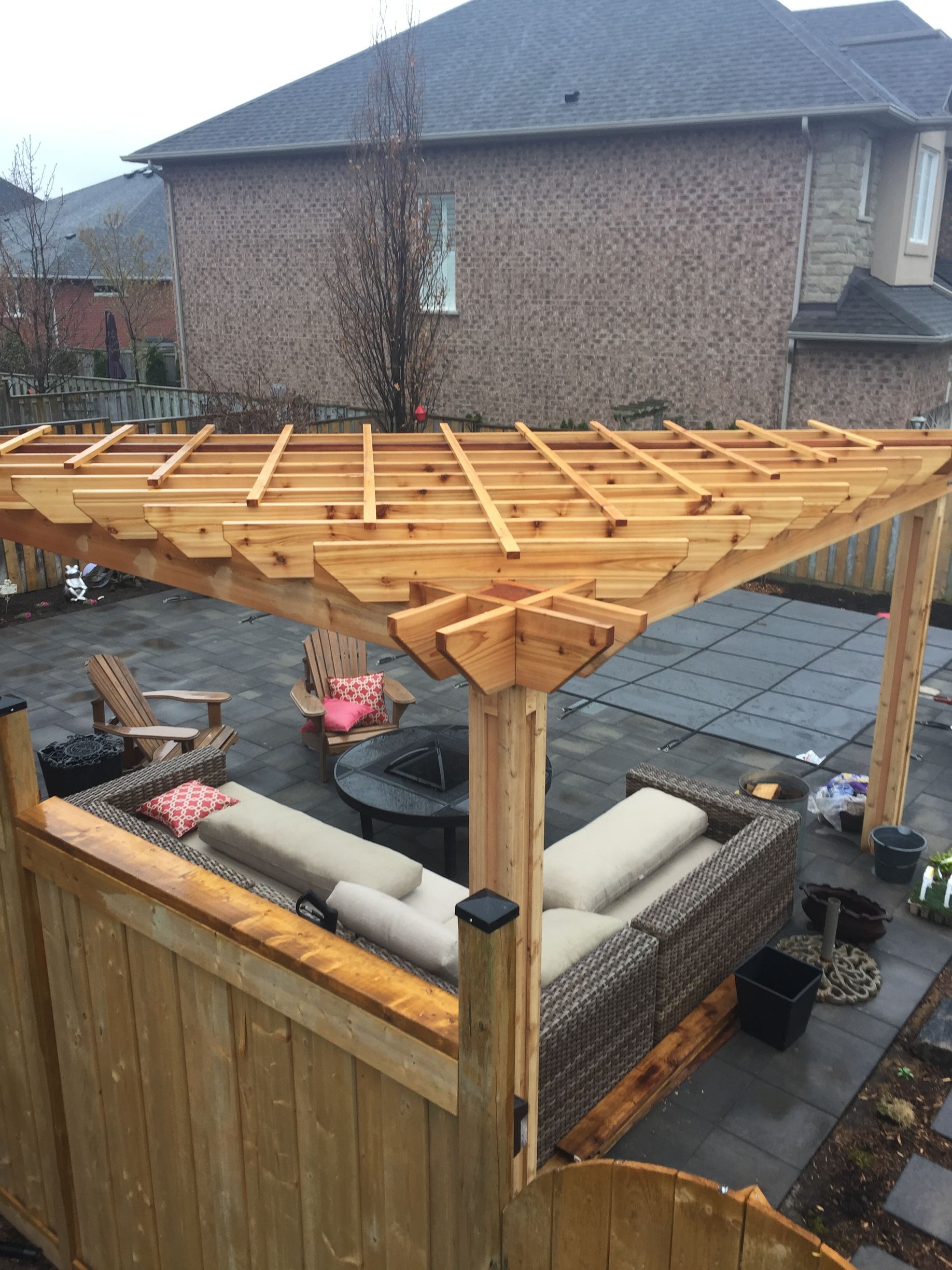 A wooden pergola is sitting on top of a patio with a couch and chairs.
