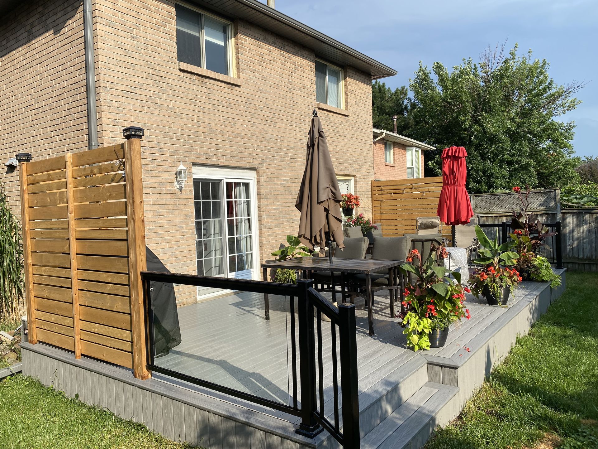 A deck with a table and chairs and umbrellas in front of a brick house.