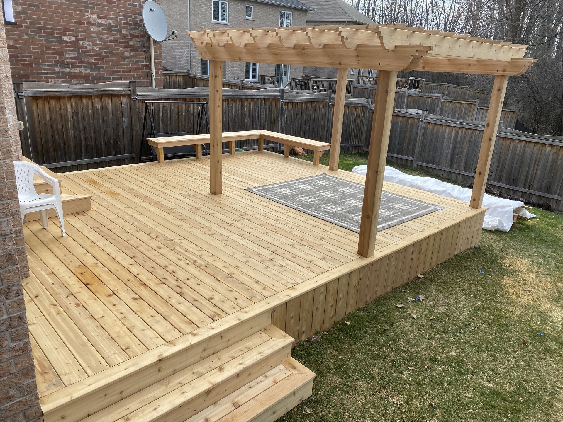A wooden deck with a pergola and benches in a backyard.