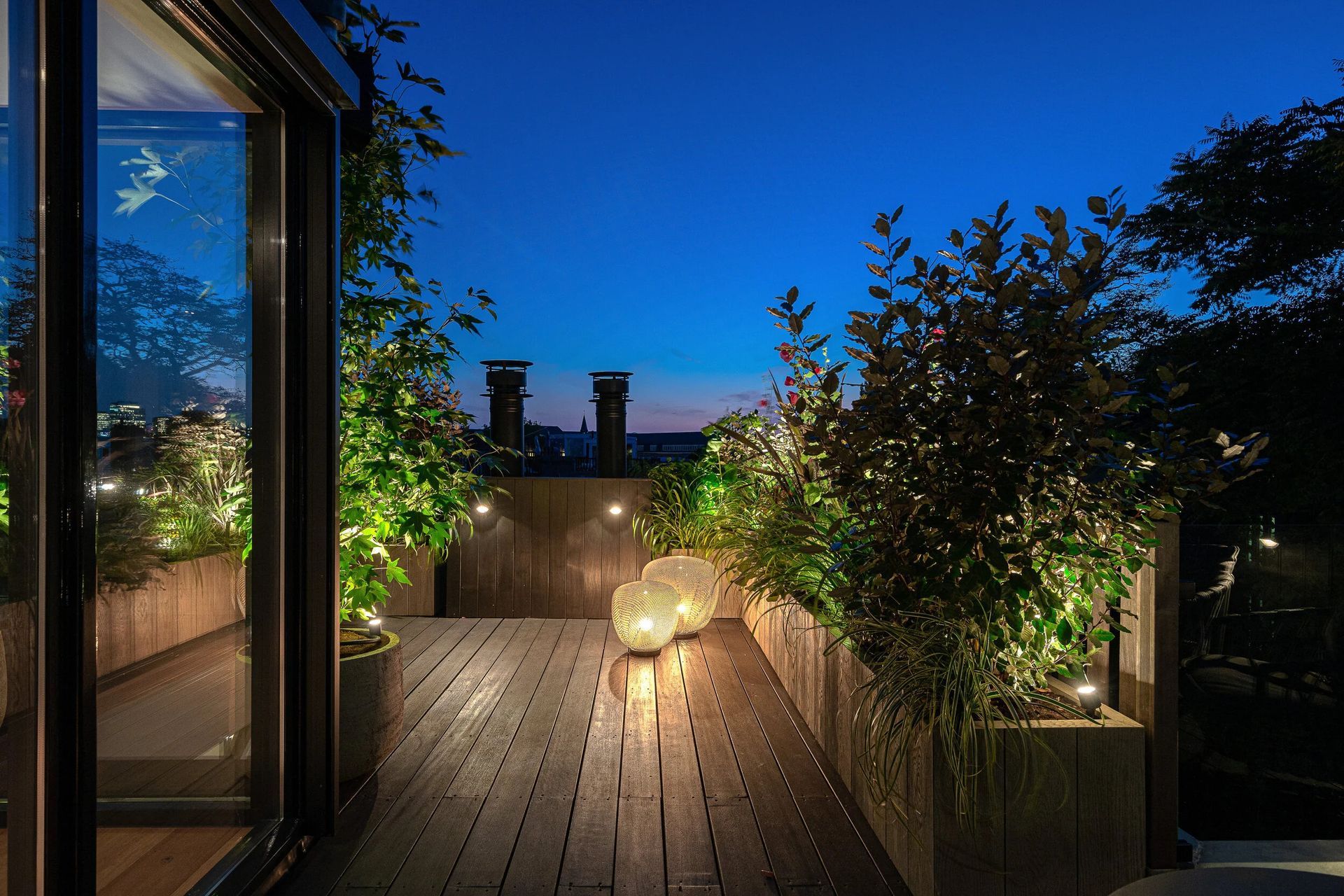Rooftop deck with lush planters and glowing lights at dusk.