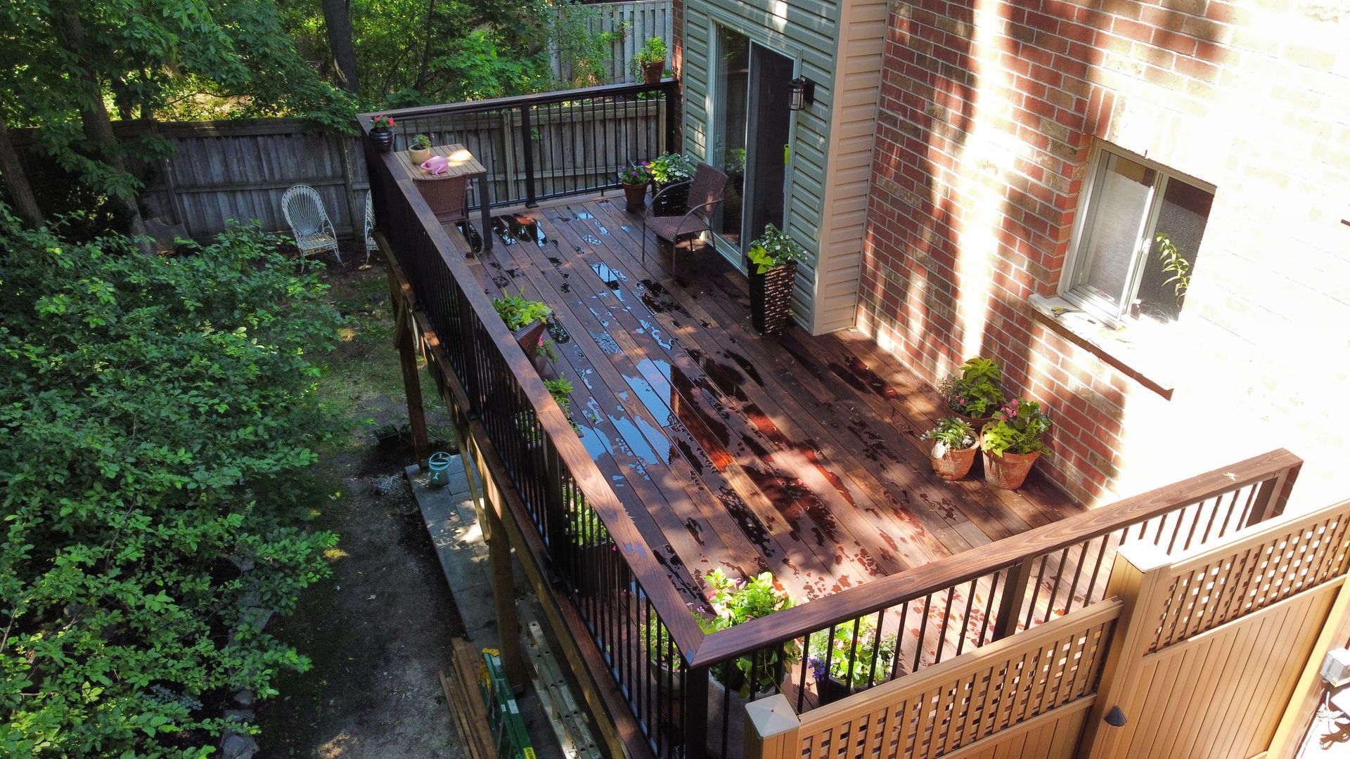 Elevated deck with wet wood planks and potted plants along railing.
