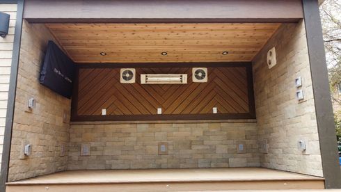 Covered outdoor space with wooden ceiling and accent wall, stone wall. Features a TV, two fans, and a heater.