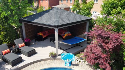 Gazebo by pool with lounge chairs, hammock, and seating. Red-leafed tree and shrubs surround the area.
