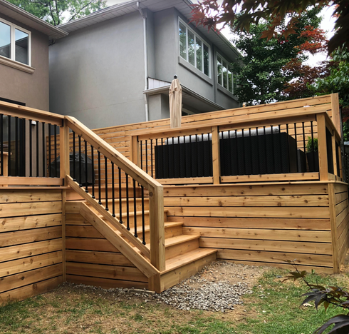 Wooden deck with stairs, black railing, and partial privacy screen. Backyard setting.