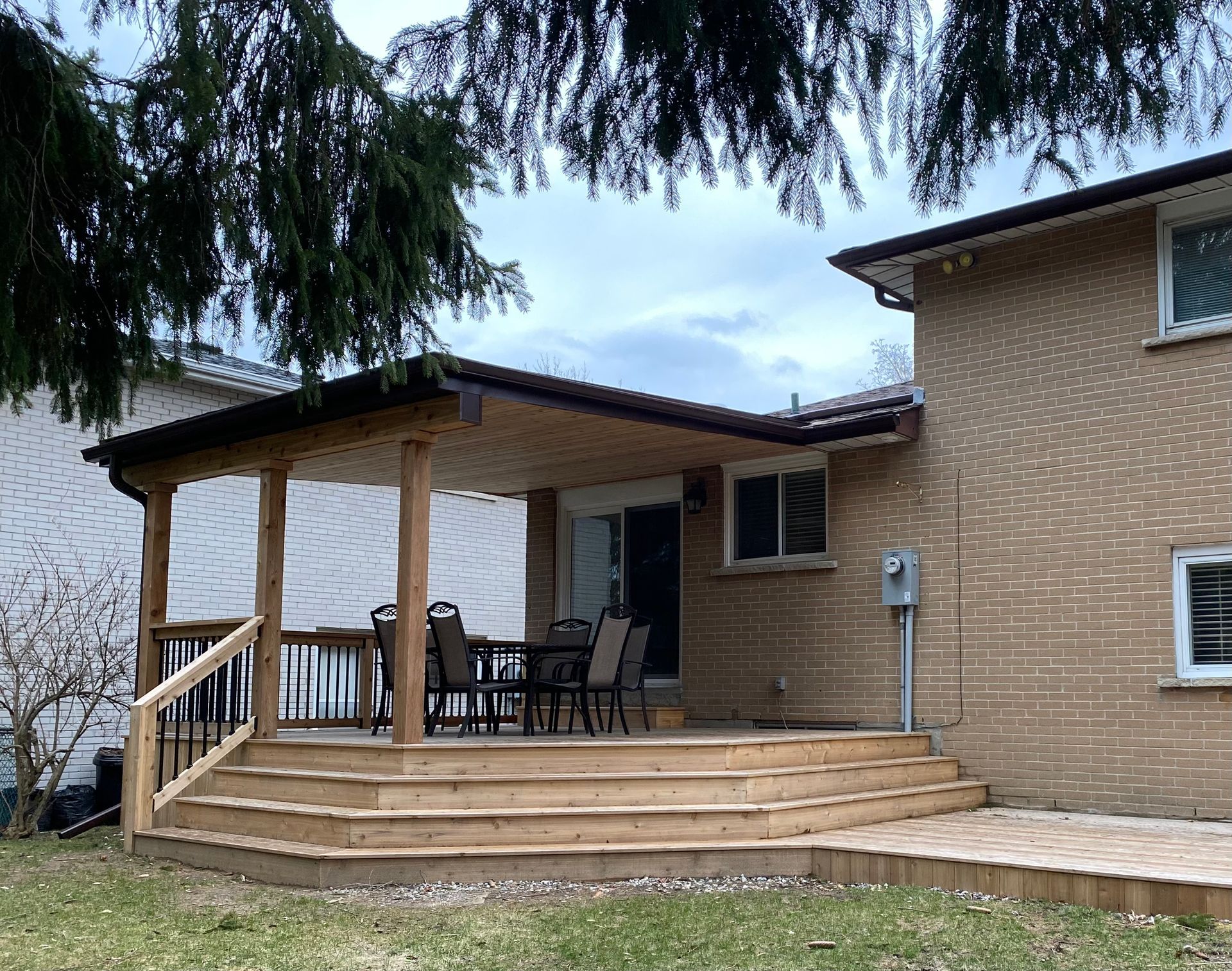 Back patio with wooden steps, covered porch, and patio chairs beside a brick house