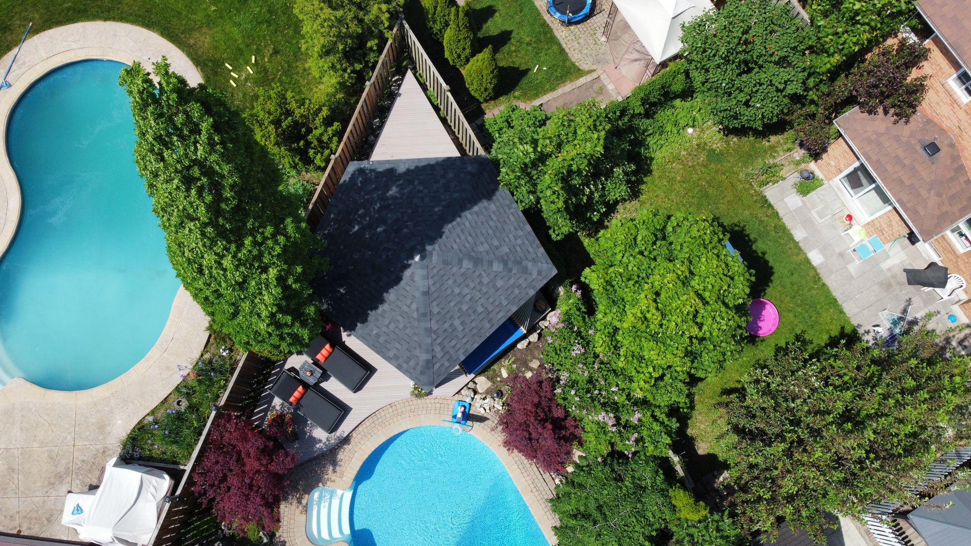 Aerial view of backyard with two pools, a gazebo, and surrounding trees.