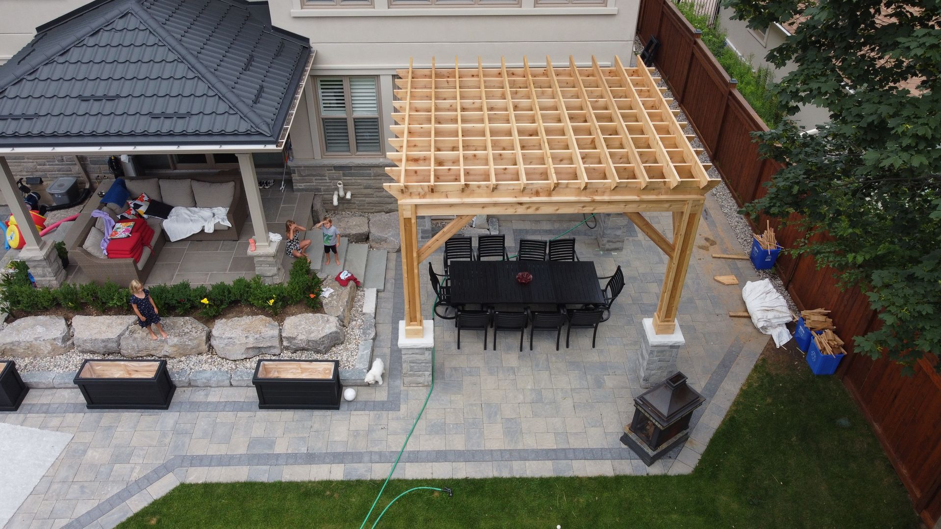 Backyard patio with wooden pergola, dining set, and surrounding landscaping.