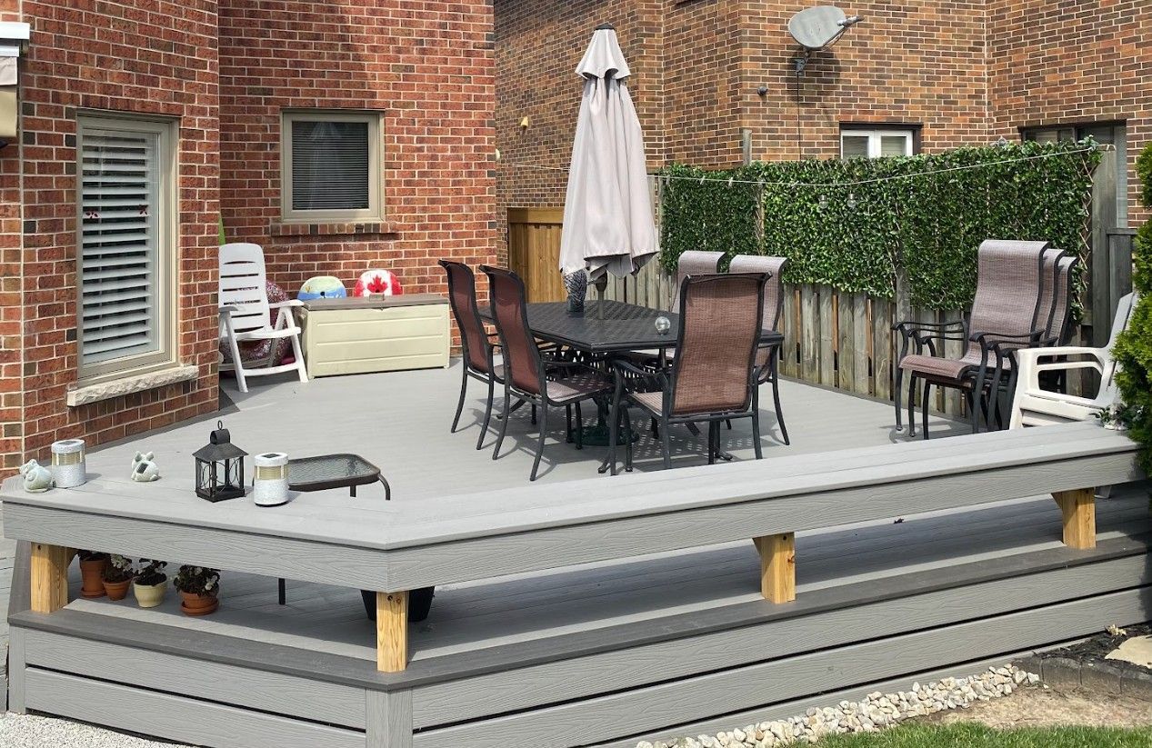 Overhead view of a gray composite deck with outdoor furniture, a grill, and surrounding landscaping.
