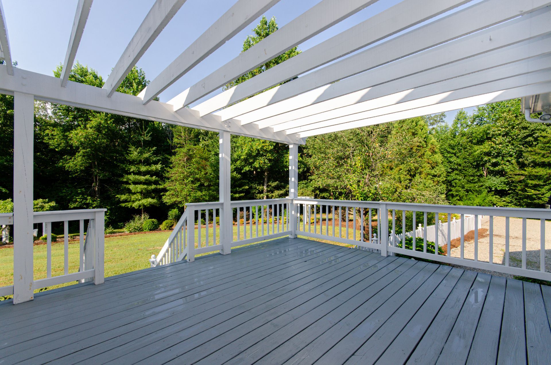 White wooden deck with pergola beams overlooking a green backyard and trees